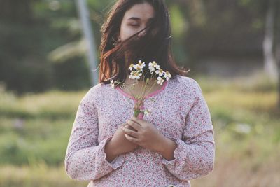 Woman holding flowers while standing on field