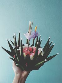 Close-up of hand holding artificial flower against blue wall
