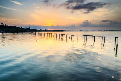 Wooden posts in sea against sky during sunset