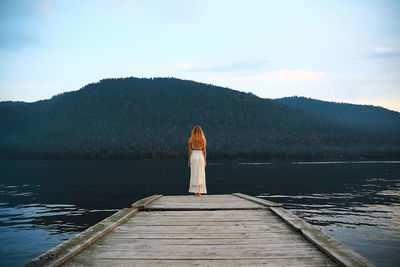 Rear view of woman on pier over lake against sky