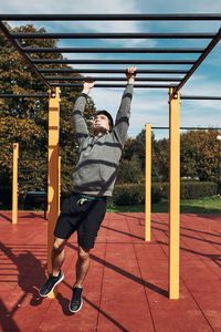 Young man bodybuilder exercising on monkey bars during his workout in a calisthenics park