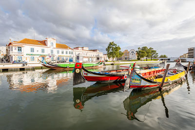 Fishing boats moored in river by buildings against sky