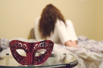 Close-up of mask on table with woman sitting on bed in background