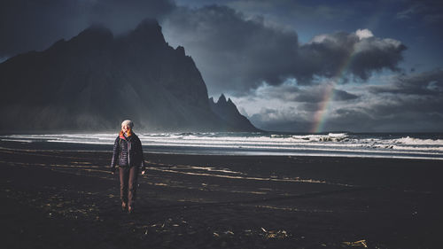 Smiling young woman standing on beach against sky