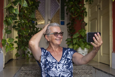 Cheerful senior woman taking selfie on steps at home