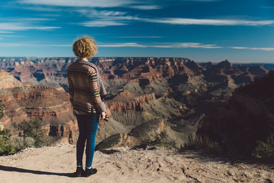 Rear view of woman standing on rock formation against sky