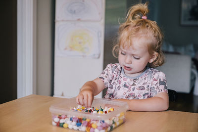 Girl with beads in box on table at home