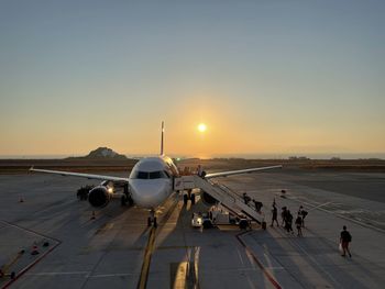 Airplane on airport runway against sky during sunset