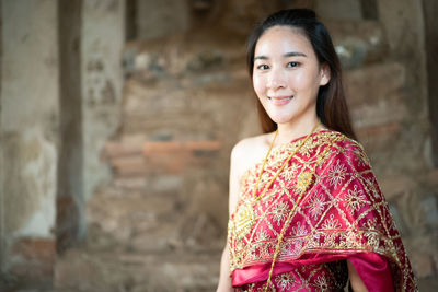 Portrait of woman smiling while standing in traditional clothing against wall