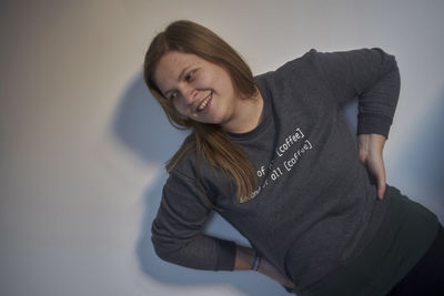 Tilt image of smiling woman with hands on hip standing against wall