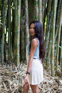 Side view of young woman looking away while standing against bamboo grove