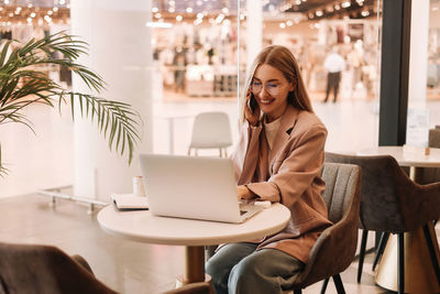 A business woman with glasses works and studies online using a mobile phone and technology in a cafe