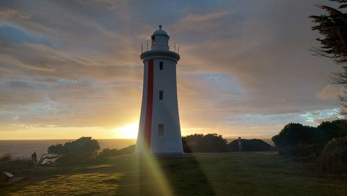 Lighthouse by sea against sky during sunset