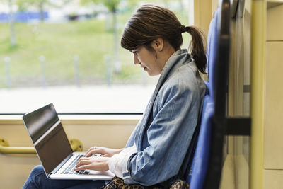 Side view of young woman using laptop in tram