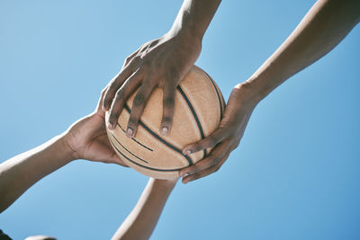 Low angle view of hand holding basketball hoop against clear blue sky