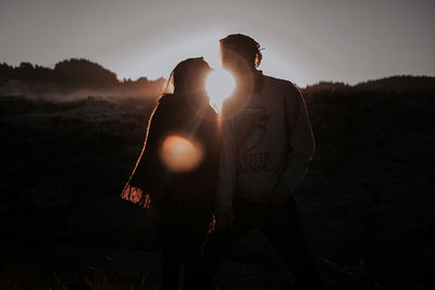 Silhouette couple standing on field against sky at night