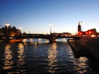 Illuminated bridge over river against sky at dusk