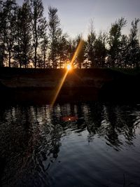 Sunlight streaming through trees on lake during sunset