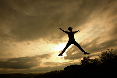 Silhouette man with arms outstretched against sky during sunset