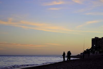 Silhouette people fishing at sea shore against sky during sunset