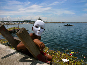 Portrait of shirtless boy wearing mask sitting on ladder by sea