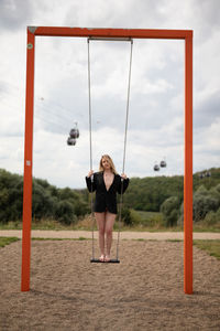 Full length portrait of woman standing on swing against sky