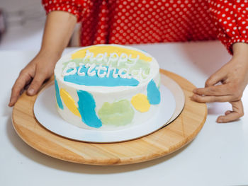 White birthday homemade cake on a wooden stand with woman's hands