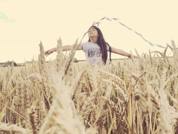 Woman with arms outstretched standing amidst agricultural field against sky