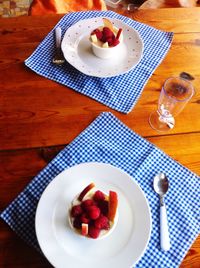 High angle view of raspberries in cup on plate at wooden table