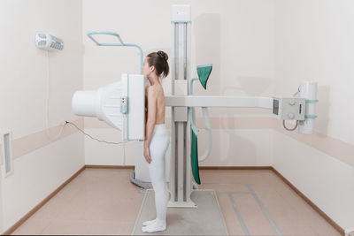 Side view of woman standing by scanning machine at clinic