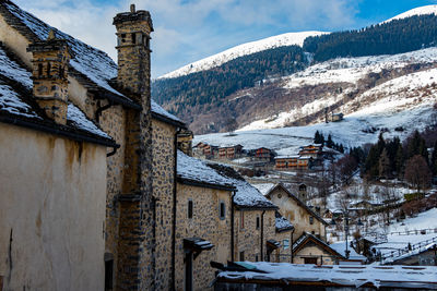 Snow covered houses by buildings against sky