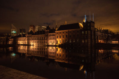 Illuminated buildings by river against sky at night