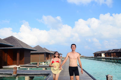 Couple walking on pier over sea against sky