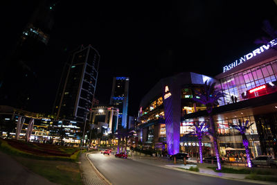 Illuminated city street and buildings against sky at night