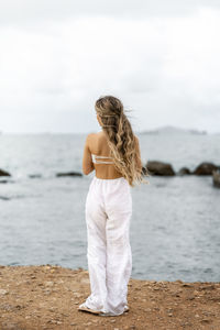 Rear view of woman standing at beach against sky