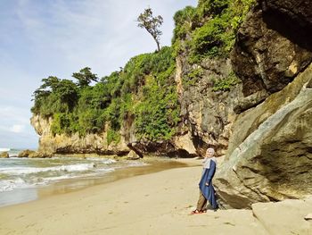 Woman on rock at beach against sky