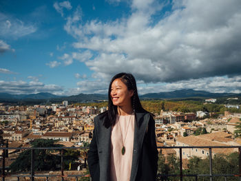 Portrait of a smiling young woman in city against sky