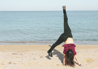 Woman doing cartwheel dance on shore at beach against sky