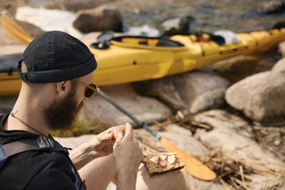 High angle view of man sitting at sea near kayak and preparing food