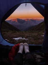 Low section of man in tent on mountain against sky during sunset