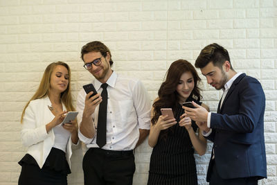 Business colleagues using phones while standing against white brick wall