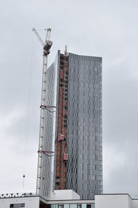 Low angle view of crane by building against sky