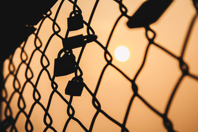 Low angle view of silhouette chainlink fence against sky during sunset