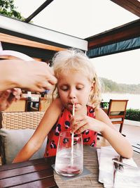 Cute girl drinking water while sitting on table at cafe