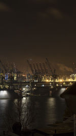 Illuminated harbor by river against sky at night