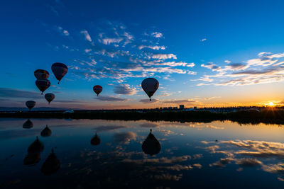 Hot air balloons in lake against sky during sunset