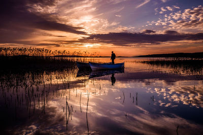 Silhouette man on boat at lake against sky during sunset