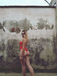 Portrait of seductive woman wearing red one piece swimsuit standing against wall