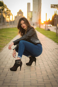 Portrait of young woman wearing high heels crouching on footpath