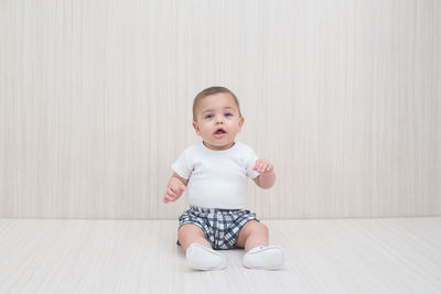 Portrait of cute girl sitting against wall